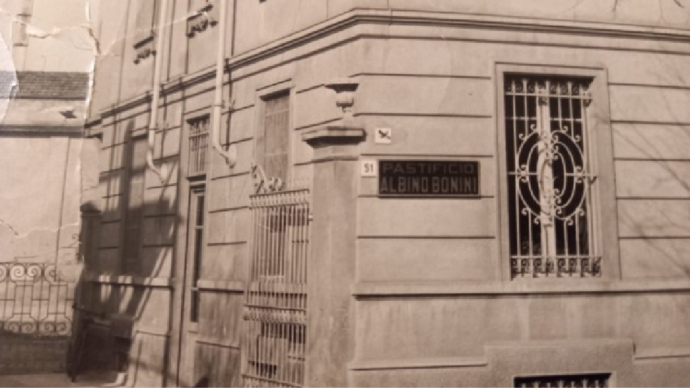 Foto storica in bianco e nero del palazzo dove è nato l'Ambulatorio Veterinario Botti Maggi. In primo piano l'insegna del Pastificio Albino Bonini, attività presente precedentemente all'apertura dell'ambulatorio veterinario